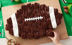 a football shaped cake on a cutting board with chocolate icing and decorations around it