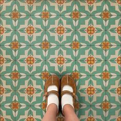 a person's feet in brown shoes standing next to a green and white tiled floor