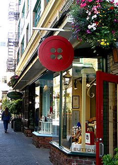 a woman walking down the street in front of a store with flowers hanging from it's windows