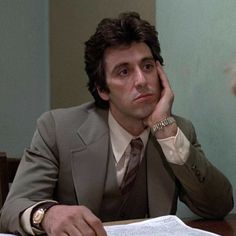 a man in a suit sitting at a table with papers and pens on his desk