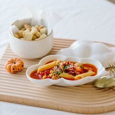 a bowl of pasta with sauce on a tray next to a fork and some small pumpkins