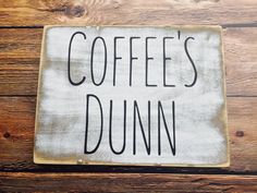 a sign that says coffee's dunn on top of a wooden table next to a cup of coffee