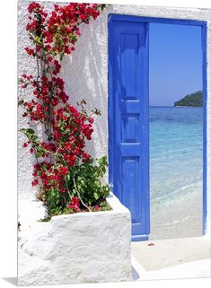 an open blue door with red flowers on the side of it and water in the background