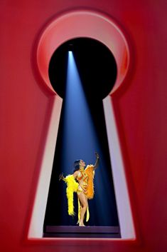 a woman is performing on stage in front of a keyhole with light coming from it