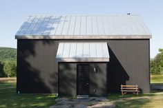 a black building with a metal roof and wooden bench in front of it on the grass