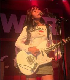 a woman standing in front of a microphone while holding a guitar