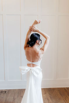 the back of a woman in a white dress with her hands on her head and arms above her head