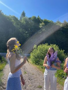 two women are standing on a dirt road and one is holding flowers in her hand