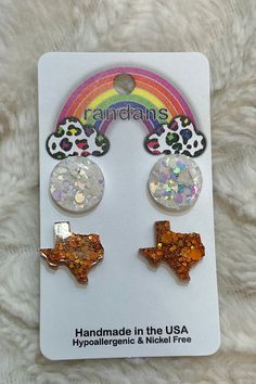 two pairs of earrings in the shape of texas and rainbows on top of each other