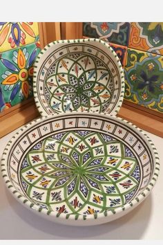 two decorative plates sitting on top of a counter next to each other in front of colorful tiles