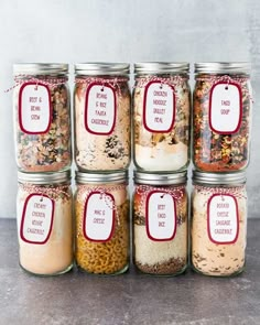 six jars filled with different types of food and labeled labels on the lids, sitting on a table