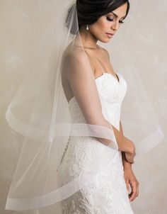 a woman in a wedding dress wearing a white veil and holding her hand on her hip