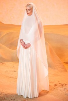 a woman in a white dress and veil standing in the desert with her hands on her hips