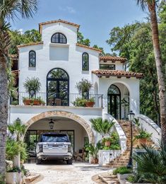 a truck is parked in front of a large white house with palm trees around it