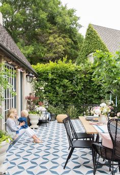 two children are sitting on the back patio with an outdoor table and chairs in front of them