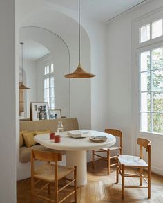 a white table and chairs in a room with wooden floors, arched windows, and a circular mirror on the wall