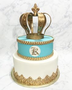 a blue and white cake with a gold crown on top is sitting on a marble table