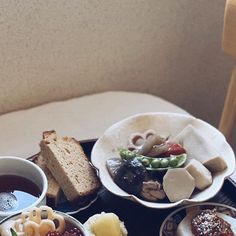 an assortment of food is on a tray next to a cup of tea and bread