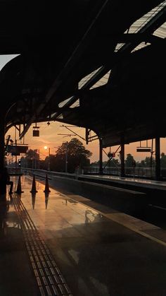 the sun is setting at an empty train station as people are walking on the platform