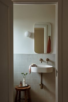 a white sink sitting under a bathroom mirror next to a wooden stool with flowers on it