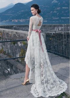 a woman standing on top of a stone wall wearing a white dress and gold shoes