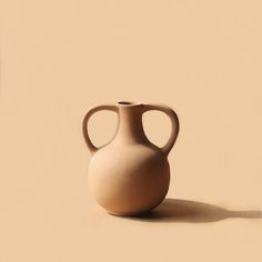 a white vase sitting on top of a beige floor next to a wall with a shadow