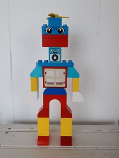 a toy robot made out of legos sitting on top of a wooden table next to a white wall