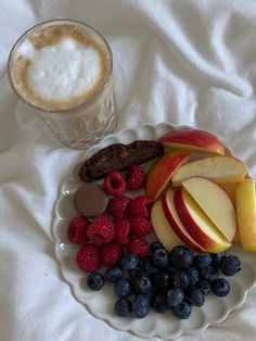 an apple, raspberries, and cookies on a plate next to a cup of coffee