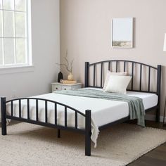 a black metal bed frame with white sheets and pillows on it in a light colored bedroom