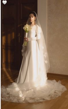 a woman in a white wedding dress holding a bouquet and standing next to a doorway