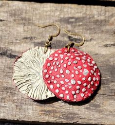 a pair of earrings with red and white polka dots on them sitting on a piece of wood