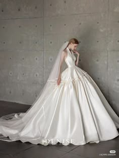 a woman in a white wedding dress standing next to a wall with her hand on her face