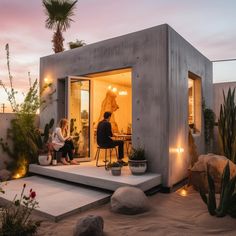 two people are sitting on the steps in front of a small house with plants and lights