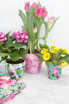 pink and yellow flowers in flower pots on a white tablecloth with napkins next to them