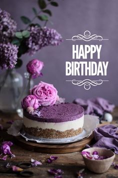 a cake with purple frosting and pink flowers on the top is sitting on a wooden table