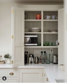 a kitchen with white cupboards filled with dishes and coffee pots on top of them