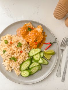 a white plate topped with rice, cucumbers and meat next to silverware