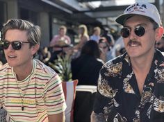 two men sitting next to each other wearing sunglasses