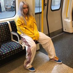 a woman sitting on a train seat with her legs crossed and wearing adidas sneakers