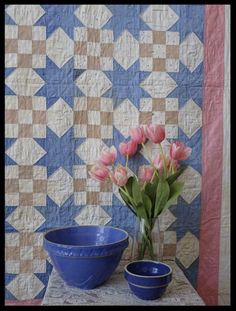 pink tulips sit in front of a blue bowl on a table next to a quilt