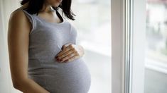 a pregnant woman standing in front of a window holding her belly up to the side