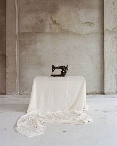 an old sewing machine sitting on top of a white table cloth covered table in front of a concrete wall