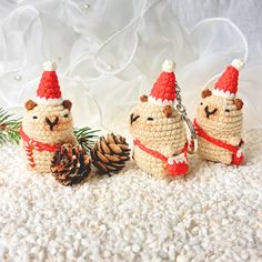 three small crocheted animals wearing christmas hats and holding pine cones, sitting next to each other