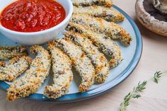 some fried food on a blue plate with a bowl of tomato sauce and mushrooms in the background