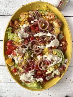 a yellow bowl filled with salad on top of a white wooden table next to a fork