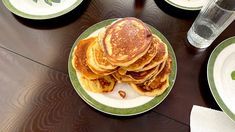 pancakes are stacked on top of each other on a table with plates and glasses next to them