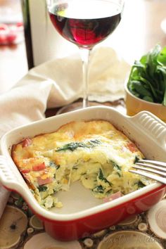 a casserole dish with spinach and cheese in it next to a glass of red wine