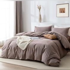 a bed with pillows and blankets on top of it next to a window in a white room