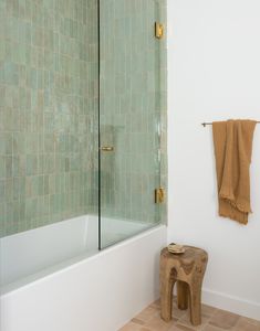 a bathroom with green tiles and a wooden stool in the corner next to the bathtub