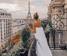 a woman in white dress looking at the eiffel tower from her apartment balcony